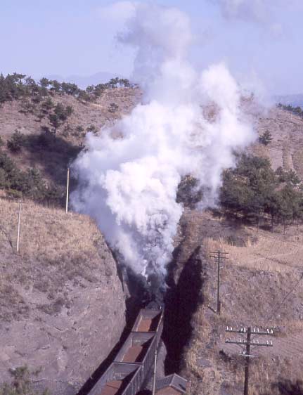 A SY 2-8-2 and a JS 2-8-2 bank a steel works bound train between the first and second tunnel on the Chengde steelworks branch. February 1999.